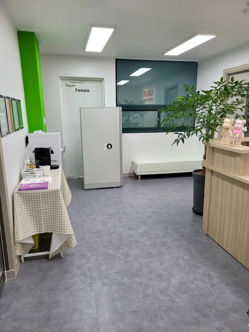 연두색 기둥과 흰 벤치, 화분이 놓인 회색 타일 바닥의 반여점 로비