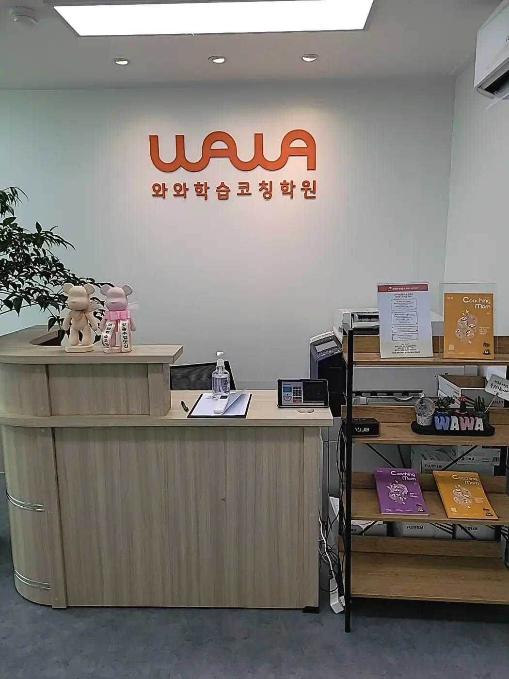주황색 WAWA 로고가 걸린 흰 벽 앞 원목 안내 데스크와 코칭맘 책자 선반이 있는 반여점 입구