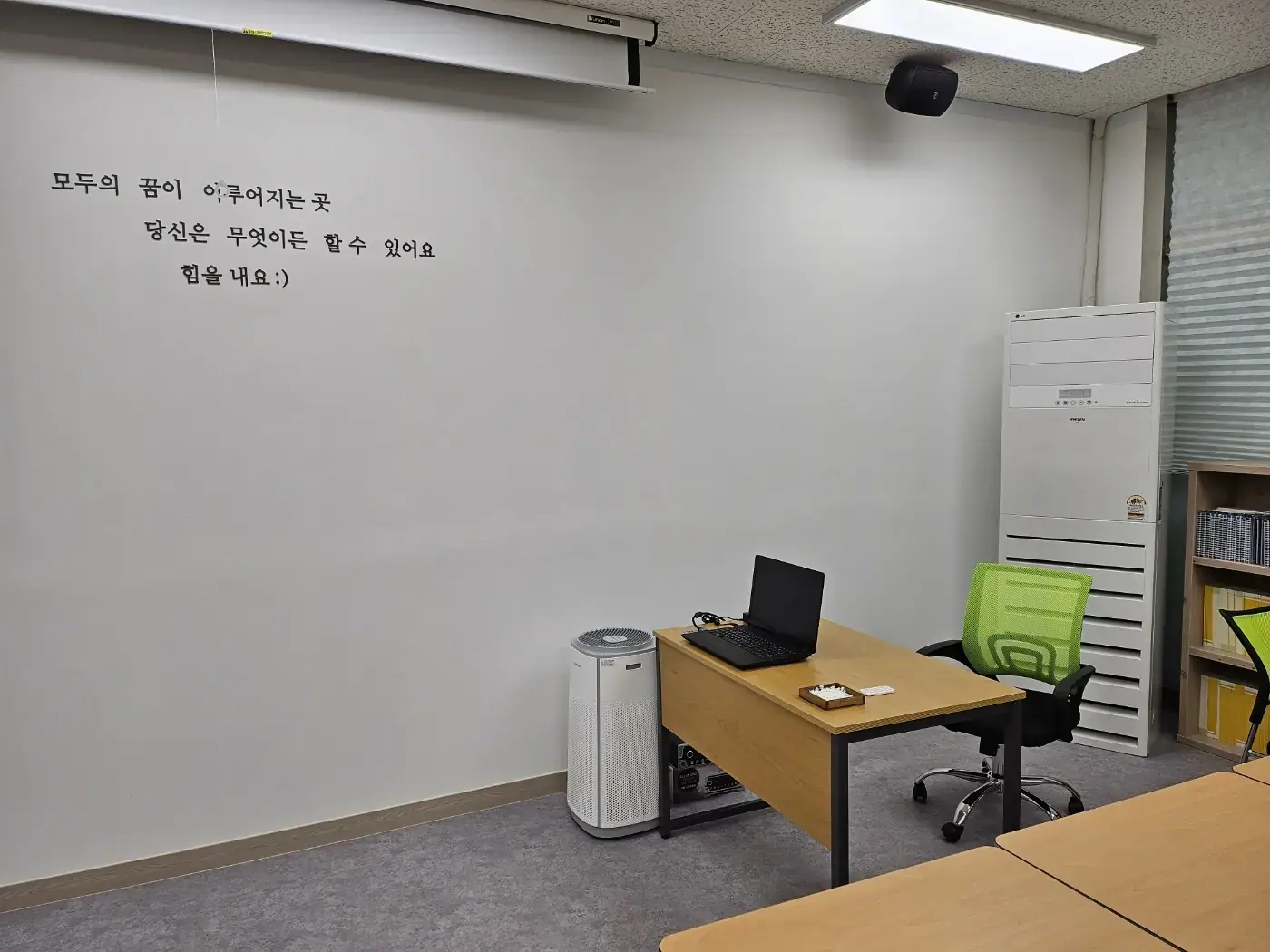 응원 문구가 적힌 흰 벽 앞 선생님 책상이 있는 웰카운티점 강의실