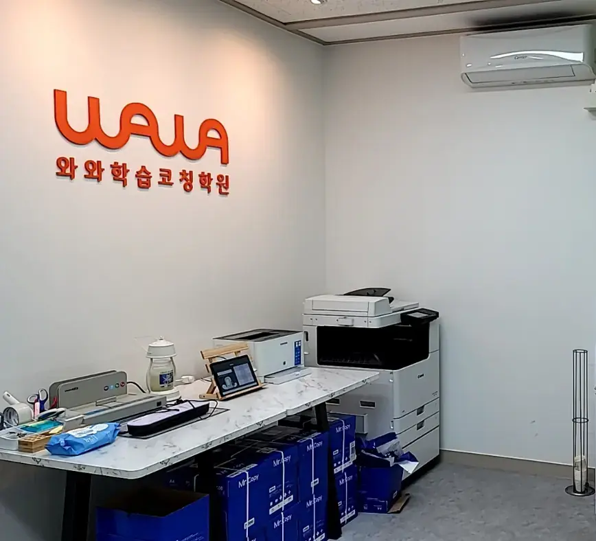 주황색 와와 로고 벽면 아래 복합기와 데스크가 놓인 퇴계원점 안내 공간