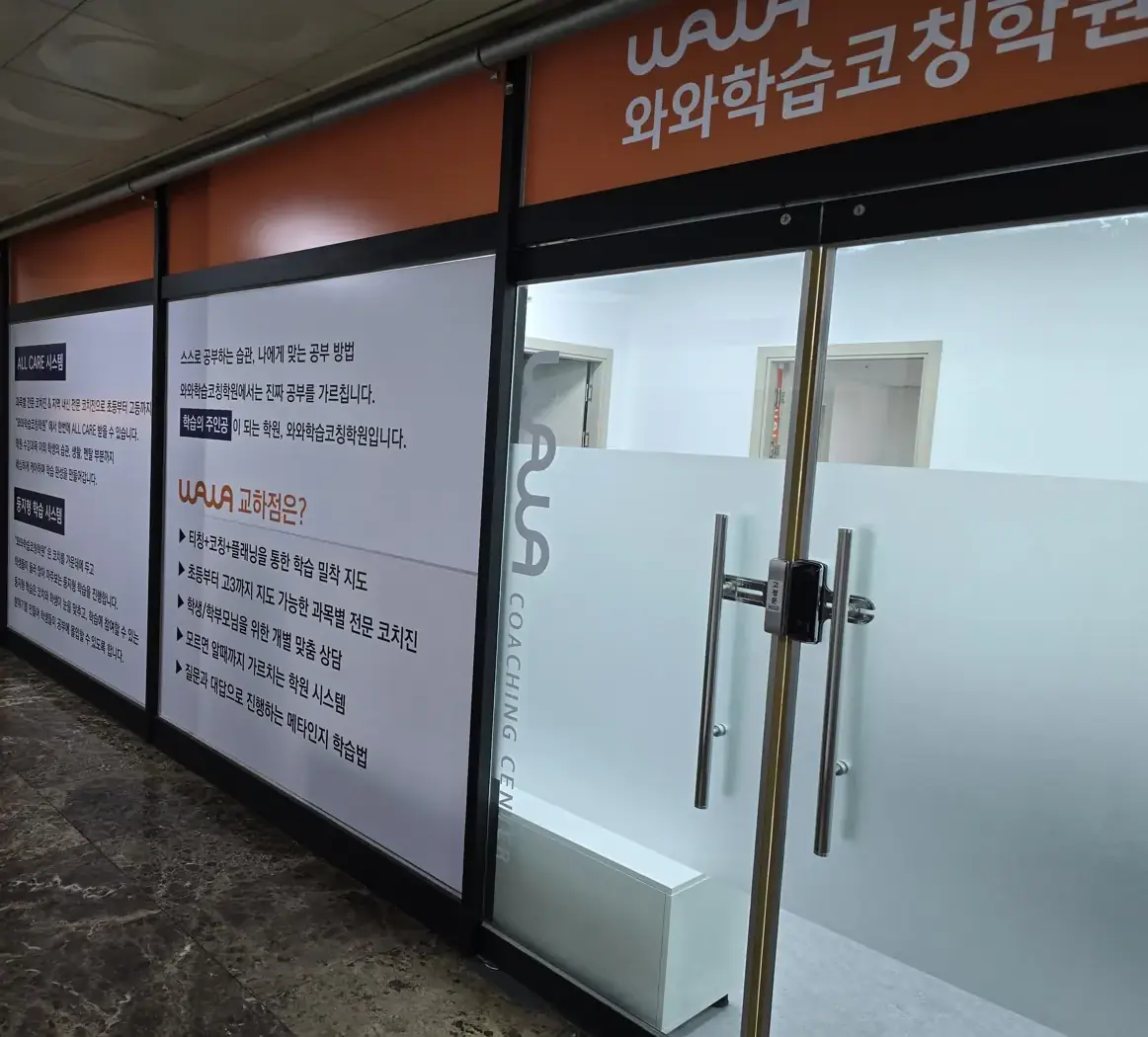 주황색 간판과 학습 안내 시트지가 붙은 유리 출입문이 있는 교하점 상가 복도 입구