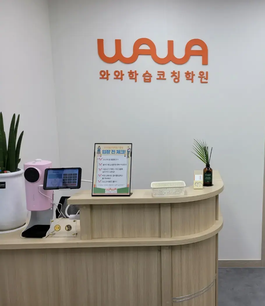 주황색 WAWA 로고와 와와학습코칭학원 글자가 붙은 벽 앞 원목 안내 데스크가 있는 이충점 입구