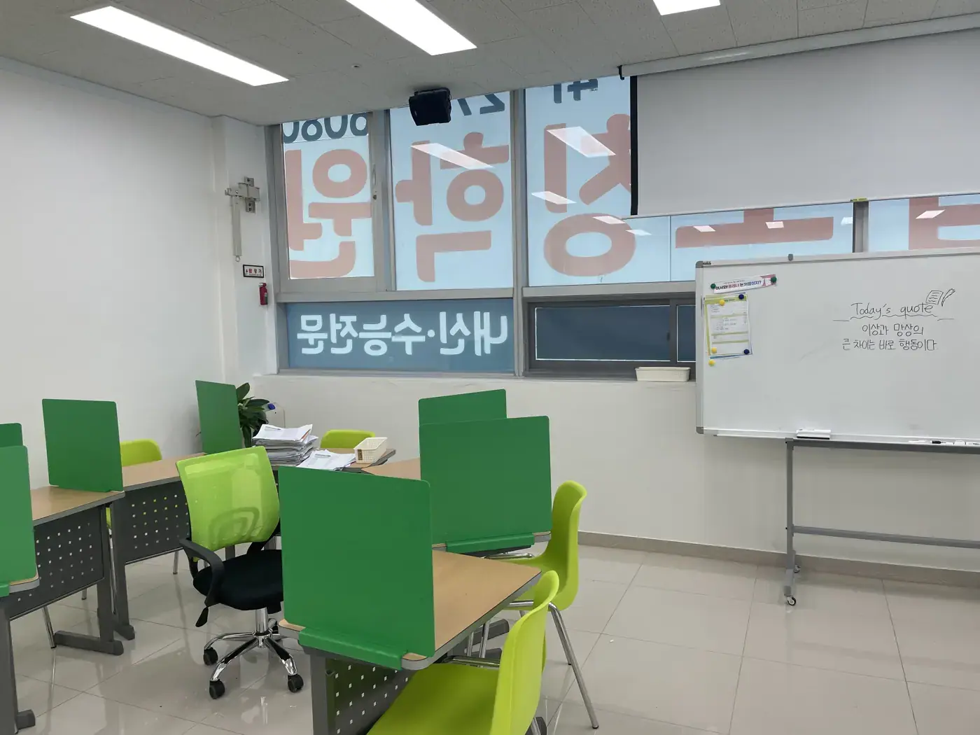 Today's quote가 적힌 화이트보드와 초록 칸막이 책상이 있는 남외점 교실